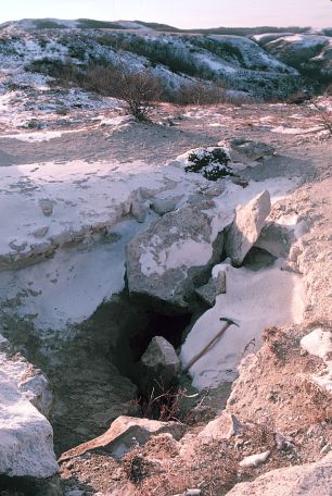 Medicine Hole in winter. This photograph was taken in 1985. In more recent years the rocks that were placed over part of the entrance to discourage cavers have been removed. 
								Spelunker Jerry Forney noted while exploring Medicine Hole that there was a pile of pebbles on the floor of the cave below the opening which had formed from people over the years dropping pebbles 
								to test the depth of the 70 foot-deep crack. 